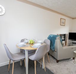A dining table set with plates and glasses next to a living area with a sofa and television at Cae Ffynnon in Star near Gaerwen