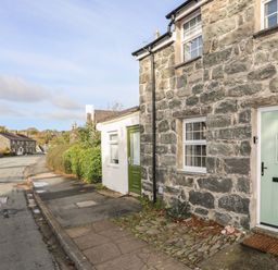 A stone house with a green door and windows next to a sidewalk along a street at Ty Eiddew Ivy House in Llanystumdwy near Criccieth
