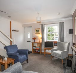 A sitting room with armchairs a small table bookshelf and a fireplace at Ty Eiddew Ivy House Llanystumdwy near Criccieth