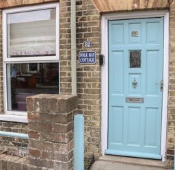 A brick cottage exterior with a blue door numbered 52 and a window next to it at Sole Bay Cottage in Lowestoft