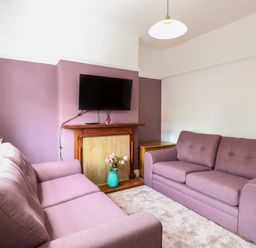 A living room with two purple sofas a wall mounted television a wooden fireplace and a vase of flowers at Sole Bay Cottage in Lowestoft