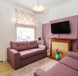 A living room with two purple sofas a wall-mounted TV and a vase with flowers at Sole Bay Cottage in Lowestoft