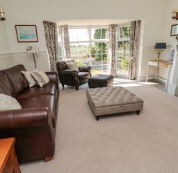 A living room with leather sofa armchair ottoman fireplace and large window at 9 Station Cottages in Belford