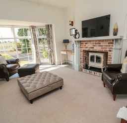 A living room with leather armchairs a television above a brick fireplace and large windows at 9 Station Cottages in Belford