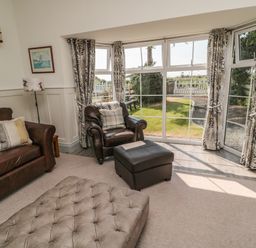 A living room with a leather sofa and armchair by bay windows with patterned curtains at 9 Station Cottages in Belford
