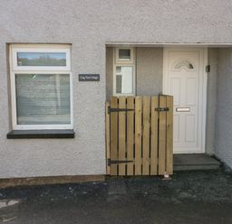 A white front door with a small wooden gate and a window on a textured exterior wall at Crag View Cottage in Stainton with Adgarley near Dalton-In-Furness