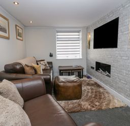 A living room with brown leather sofas a wall-mounted television a fireplace and a window with striped blinds at Crag View Cottage in Stainton with Adgarley near Dalton-In-Furness