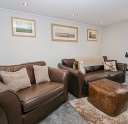 A living room with brown leather sofas, an ottoman, framed pictures on the wall, and nested side tables at Crag View Cottage in Stainton with Adgarley near Dalton-In-Furness