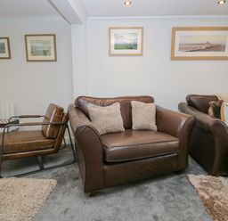 A living room with leather armchairs and a sofa with cushions on a carpet with framed pictures on the wall at Crag View Cottage in Stainton with Adgarley near Dalton-In-Furness