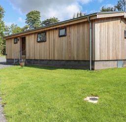 A single-story wooden house with small windows on a grass lawn at Corning Mill View in Haverthwaite