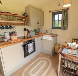 A kitchen with a wooden countertop a sink oven toaster kettle and a small dining table with chairs at Sheep Cote Shepherds Hut in Chop Gate near Stokesley