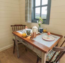 A small dining table set for two with eggs, mugs, orange juice, and toast near a window at Sheep Cote Shepherds Hut in Chop Gate near Stokesley