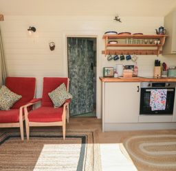 A kitchen area with two red chairs and a door in the middle at Sheep Cote Shepherds Hut Chop Gate near Stokesley