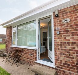 The entrance of a brick house with an open white door a small wooden table and two chairs outside at 8 Royal Chalet Park in Mundesley