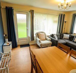 A living room with a dining table chairs a sofa an armchair and a door at 8 Royal Chalet Park in Mundesley