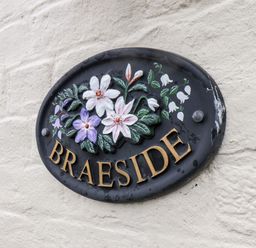 A black oval plaque with flowers and the word Braeside on a textured wall at Braeside in Fylingthorpe