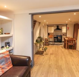 A living room with a leather sofa and an open view into a kitchen with a dining table at Lime Court Barn in Sheepwash