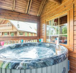 An outdoor hot tub on a wooden porch with colored glasses and a bottle at Robin Lodge in Llanbedr