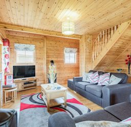 A living room with gray sofas a wooden coffee table a TV and wooden staircase at Robin Lodge in Llanbedr