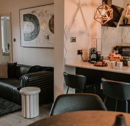 A living area with a black ribbed sofa and cushions next to a kitchen with bar stools and a countertop at 37 Jubilee Street in Llandudno