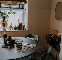 A dining area with a round table, black chairs, a window with a vase, books, and decorative items at 37 Jubilee Street in Llandudno