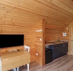 A small wooden kitchen area with a table and chairs and a wall mounted TV at Cleugh Lodge in Lockerbie
