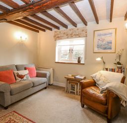 A living room with a gray sofa and brown leather armchair with wooden ceiling beams at Cosy Cottage in Bawdeswell