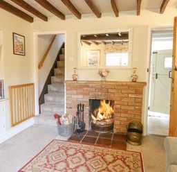 A living room with a fireplace a staircase and an open door at Cosy Cottage in Bawdeswell