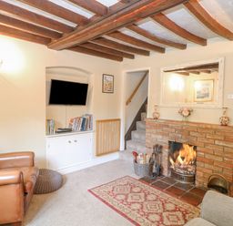 A living room with a brick fireplace a television on a built-in shelf and wooden ceiling beams at Cosy Cottage in Bawdeswell