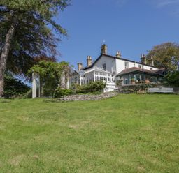 A house with a glass conservatory and stone walls on a grass slope with trees at Valley View in Dalton-In-Furness