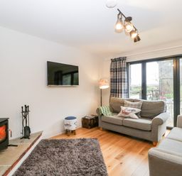 A living room with two sofas a wood burning stove and a wall mounted television at Little Stables Cottage in Spetisbury