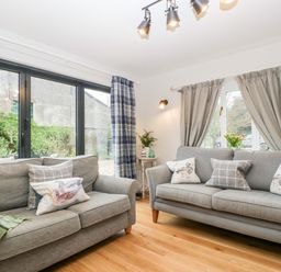 A living room with two gray sofas with patterned cushions and curtains at Little Stables Cottage in Spetisbury