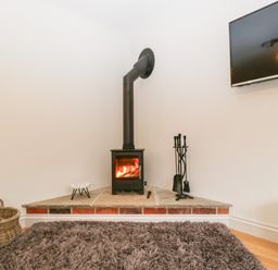 A corner with a black wood stove heating a fire a basket of logs a set of fireplace tools and a mounted tv at Little Stables Cottage in Spetisbury