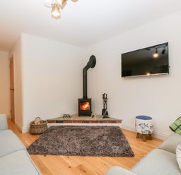 A living room with a wood burning stove a wall mounted TV and two sofas at Little Stables Cottage in Spetisbury