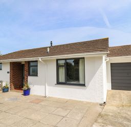 A single story house with a tiled roof a garage and potted plants on a paved area at Bryn Alaw Newport Pembrokeshire