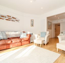 A living room with a brown leather sofa and two armchairs with footstools at Cliffside Trebarwith Strand near Tintagel