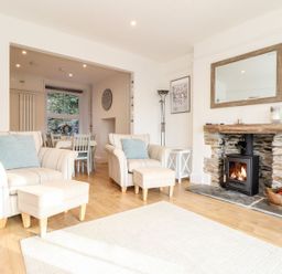 A living room with two armchairs and ottomans next to a fireplace and a dining area in the background at Cliffside in Trebarwith Strand near Tintagel
