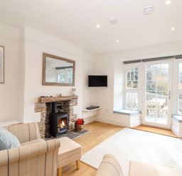 A living room with a fireplace armchairs a wall-mounted tv and large windows at Cliffside in Trebarwith Strand near Tintagel