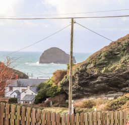 A view of rocky cliffs sea and houses behind a wooden fence at Cliffside in Trebarwith Strand near Tintagel
