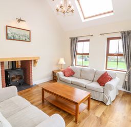 A living room with two sofas a wooden coffee table a wood stove and two windows at Ballycahane Castletownshend County Cork