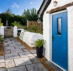 A paved path leading to a wooden gate with plants on both sides and a blue door on a white building at The Old Bakery