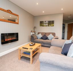 A living room with two grey sofas a wooden coffee table a wall-mounted electric fireplace and a mirror at Beech Lodge in Goosnargh
