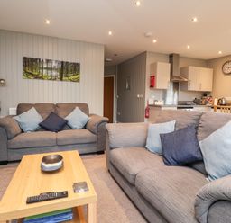 A living room with two grey sofas and a wooden coffee table adjacent to a kitchen at Beech Lodge in Goosnargh