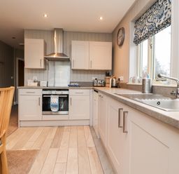A kitchen with white cabinets a stainless steel oven and hood a sink by a window and a wooden chair at Beech Lodge in Goosnargh