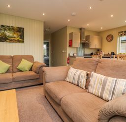 A living room with two brown sofas and cushions near a kitchen with wooden chairs and cabinets at Oak Lodge in Goosnargh