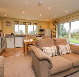 An open kitchen and dining area with a beige sofa and sliding glass doors at Oak Lodge in Goosnargh