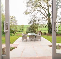 A patio with a table and four chairs looking out to a garden and trees at Court Lodge in Bathealton near Wiveliscombe