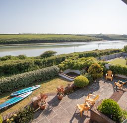 A patio with chairs and plants overlooking a river with grassy hills in the background at Newquay Tamarisk Lodge on the Gannel in Newquay
