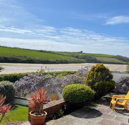 A garden patio with yellow chairs and potted plants overlooking a river and green hills at Newquay Tamarisk Lodge on the Gannel in Newquay