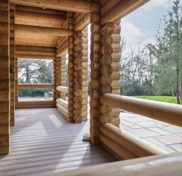 A wooden log porch overlooking a grassy area with trees at Redwood Lodge in Ellesmere